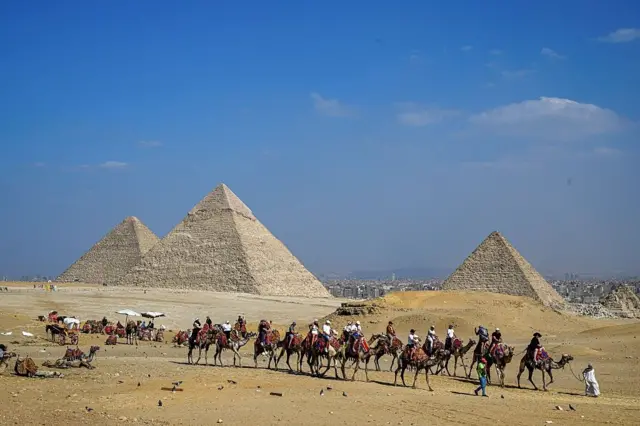 Des touristes font une promenade à dos de chameau dans la nécropole des pyramides de Gizeh, en périphérie de la ville jumelle de la capitale égyptienne, le 7 novembre 2025.