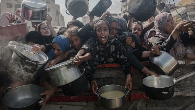 مجموعة من النساء الفلسطينيات ترتدين ملابس إسلامية الطابَع وتمسكن بأوانٍ فارغة، على أمل ملئها بالغذاء من أحد مراكز توزيع المساعدات الغذائية، وسط الحصار والهجمات الإسرائيلية المتواصلة على غزة.