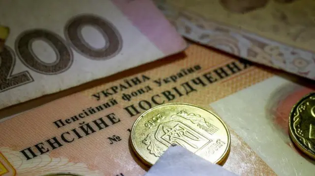 Гривневі купюри і монети лежать на пенсійному посвідченні.