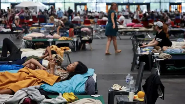 Женщина смотрит в свой телефон, лежа на раскладушке в выставочном центре «Бордо-Лак»