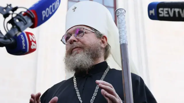 Человек в очках, священническом облачении и белой митре