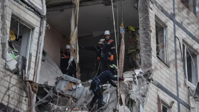 Несколько спасателей работают в разрушенной квартире в многоэтажном доме.