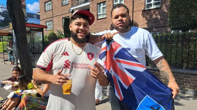 電視名廚Big Zuu(左)與好友米奇·珀金斯(Mickey Perkins)一同參加諾丁丘嘉年華慶典。Big Zuu手持飲品,身穿利物浦球衣,而他的朋友則穿著白色 T 恤並手持一面旗幟