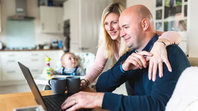 Домашній знімок, на якому молода сім'я за комп'ютером, а в вітальні сидить немовля 