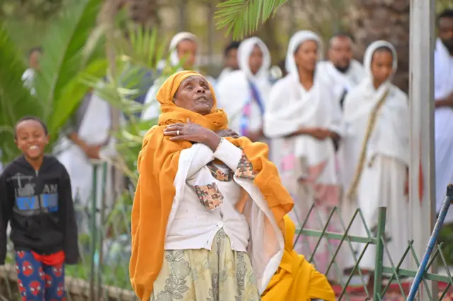 ብጫ ጋቢ ዝደረበት ኣደ ዓይና ዓሚታ ንሰማይ እናተማህለለት፡ ኣብ ድሕሪኣ ሓደ ፍሽኽታ ዝዓሰሎ ቆልዓን፡ ኣብ ጸሎት ዝርከባ ኣዴታትን ይራኣያ