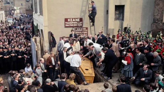 O momento em que Mick Meany foi retirado do caixão, com muitas pessoas à sua volta