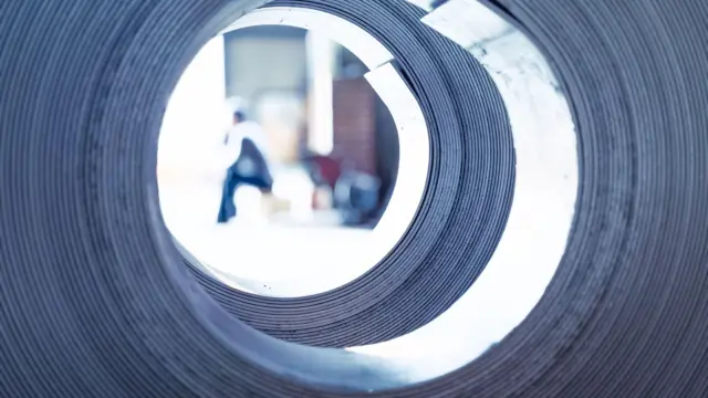 تصویری با نمای نزدیک از یک کلاف فولادی که کارگری از داخل آن در پس‌زمینه در کارخانه‌ای در هواسینونگ، در گیونگی-دو، در کره جنوبی دیده می‌شود