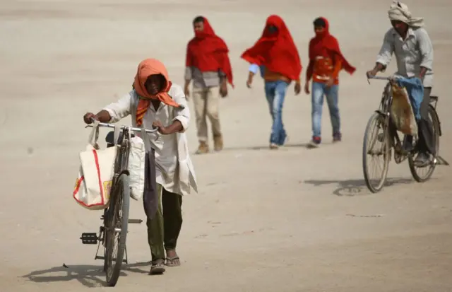 ఎండలో సైకిల్ నడుపుకుంటూ వెళ్తున్న వ్యక్తులు
