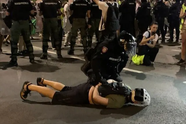 Момак са кациом лежи на земљи, а држи га полицајац