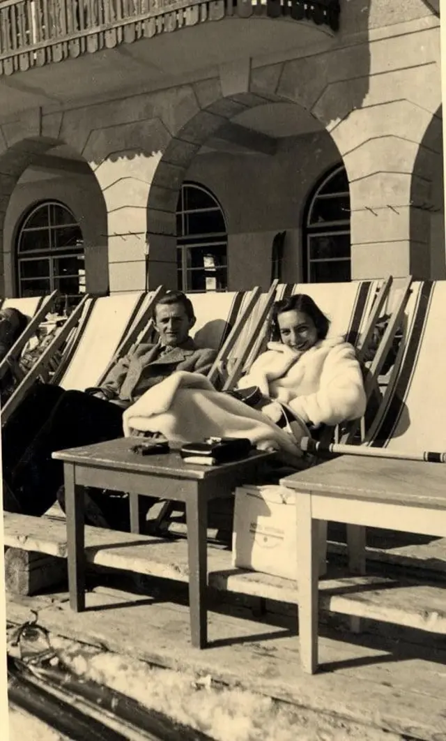 Una pareja en unas tumbonas miran sonrientes a la cámara en una imagen en blanco y negro.