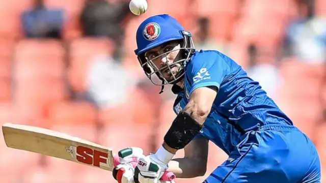 رحمان‌الله گربز هنگام توپ‌زنی با لباس آبی رنگ تیم ملی، او ویکت به دست دارد و به توپی که طرفش می‌آید خیره شده است.