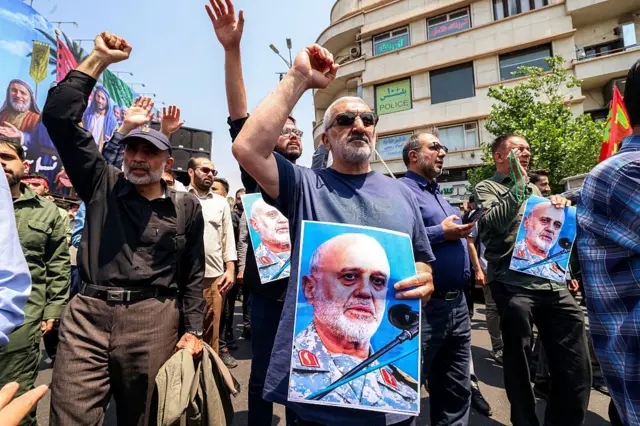 Tahran'da İranlılar srail'in saldırılarını protesto ediyor. Sağ ellerini yumruk yapıp havaya kaldırmışlar. Öndeki bir kişi Gülam Ali Reşid'in fotoğrafını taşıyor.