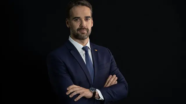 Eduardo Leite de braços cruzados e terno olhando para câmera