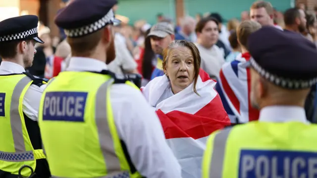 Женщина, укутанная в английский флаг, беседует с полицейскими на котр-протесте против ультраправых, протестовавших против мигрантов у гостиницы в Орпингтоне под Лондоном 22 августа 2025 года