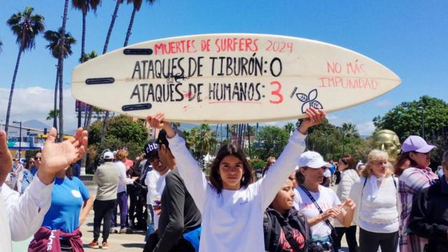 Una mujer sostiene una tabla de surf con la inscripción "Muertes de surfistas-Ataques de tiburones: 0 y Ataques humanos: 3" durante una protesta. 