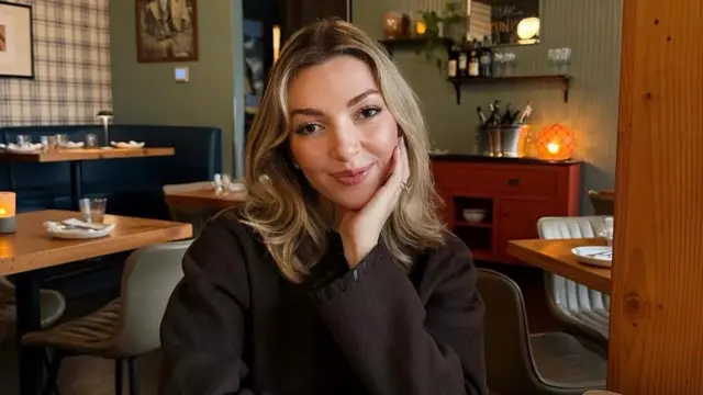 Ginger Smith, egy vállig érő szőke hajú nő egy éttermi asztalnál ül.