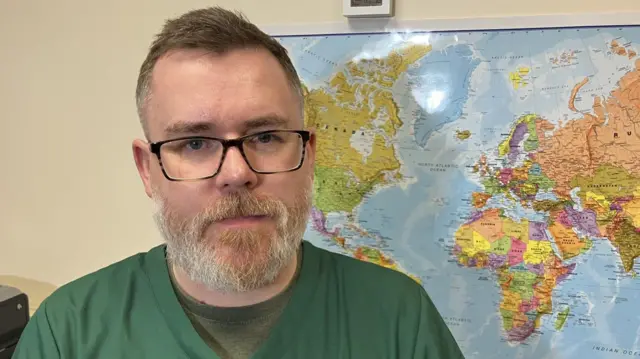 Mike Smith de pie frente a un mapa del mundo con alfileres que muestran dónde se han transportado las donaciones desde el centro de Nottingham.