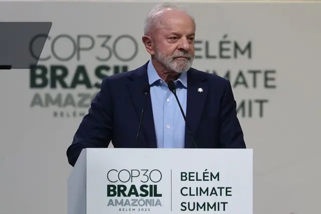 Presidente Lula falando no palco da COP30, em Belém. Ele usa um terno azul marinho. No púlpito está escrito COP30 Brasil Amazônia.