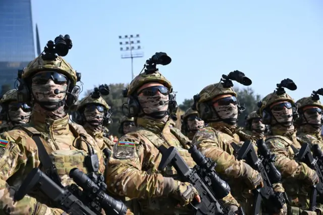 Средний план. Ряды военных в камуфлеже и с оружием.