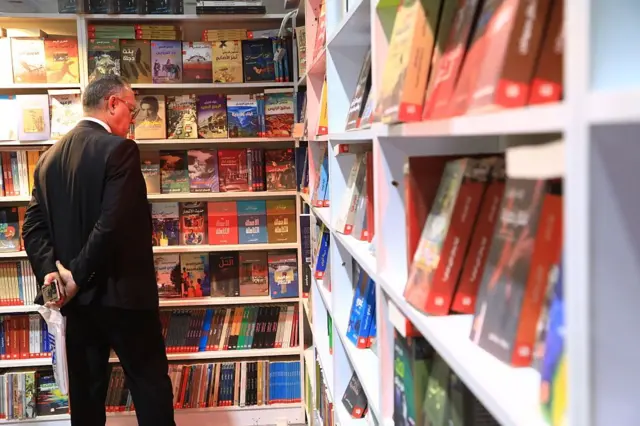Um homem observando uma prateleira cheia de livros