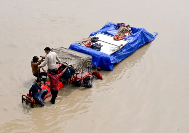 दिल्ली के मयूर विहार के पास पानी का स्तर बढ़ने के बाद सुरक्षित स्थान पर जाते लोग