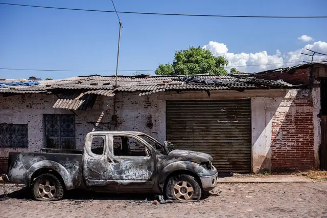 Un vehículo estilo pick up frente a un negocio con la persiana bajada en una calle adoquinada quemado después de una ola de violencia en la ciudad de Aguililla, lugar de nacimiento del capo de la droga Nemesio Oseguera, líder del Cártel de Jalisco Nueva Generación (CJNG) en Tierra Caliente, México, el 24 de febrero de 2026. (Foto de Enrique Castro / AFP vía Getty Images)