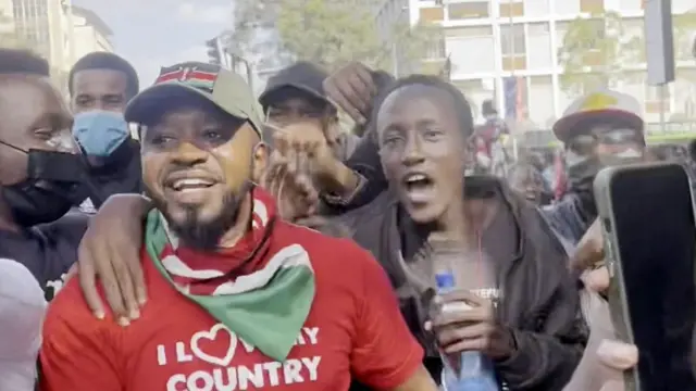 Boniface Mwangi (à gauche) avec un T-shirt rouge « J'aime mon pays » et un drapeau kenyan autour du cou - dans une foule de jeunes manifestants - 25 juin 2024