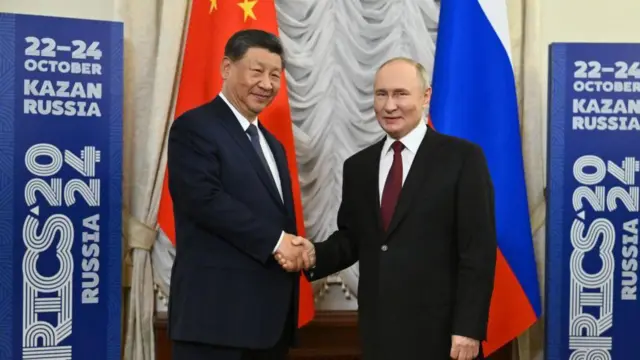ولادیمیر پوتین رئیس جمهور روسیه (راست) و شی جین پینگ، رئیس جمهور چین (چپ) هنگام شرکت در شانزدهمین اجلاس سران بریکس در کازان روسیه در ۲۲ اکتبر ۲۰۲۴ با یکدیگر دست می دهند.
