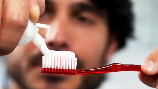 شاب يضع معجون أسنان على فرشاة استعداداً لتنظيف أسنانه