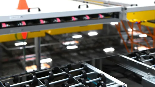 Una lámina de vidrio está pasando por una máquina con rodillos.