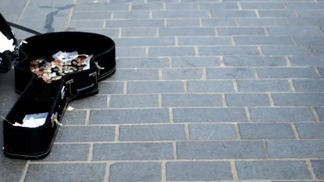 路上に開いておかれたストリートミュージシャンのギターケースに、小銭がたくさん入っている様子