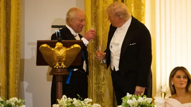 チャールズ国王とトランプ大統領がワイングラスを掲げて乾杯している。共に正装をしており、国王の隣には金色のわしの形をした演台が置かれている