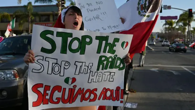 Una mujer lleva una pancarta que dice "Stop the hate. Seguimos aquí"