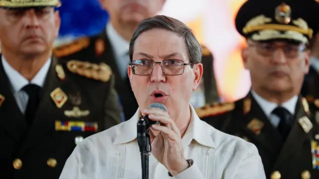 El canciller de Cuba, Bruno Rodríguez. habla ante un micrófono acompañado de oficiales militares