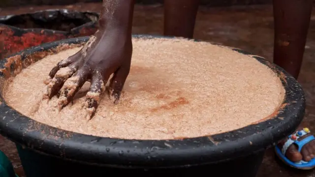 One woman dey stir shea butter paste wit her hand for plastic container in Nigeria