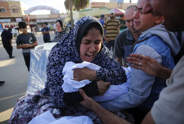 A woman sobs as she holds what appears to be the body of a child wrapped in a white shroud