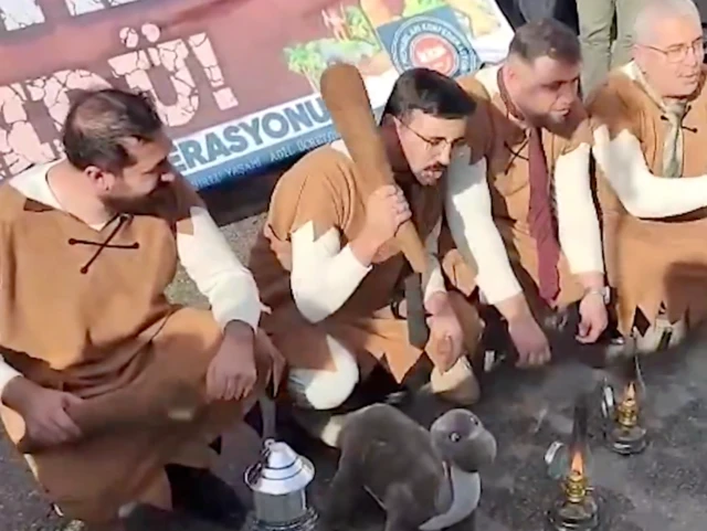 Taş Devri çizgi filmindeki kıyafetleri giymiş memurlar ve emekliler, yere çömelmiş. Ellerinde sopalar ve önlerinde oyuncak bir dinozor var.