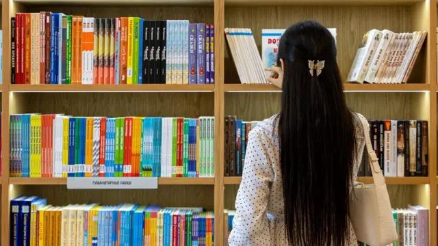 Китоб жавонидан китоб танлаётган Ўзбек қизи