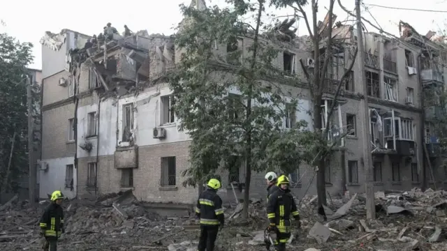 فرق أنقاذ قرب مبنى متضرر في دنيبرو ويظهر أربعة رجال أمام مبنى مدمر جزئياً