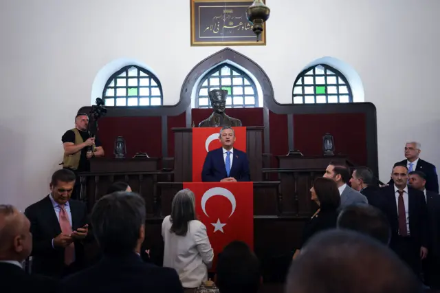 1. TBMM binasında tarihi kürsüye çıkan Özgür Özel'in çevresinde basın mensupları ve partililer toplanmış durumda.