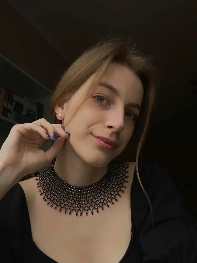 Фотопортрет дівчини в красивому намисті та чорньому верхньому одязі на темному фоні