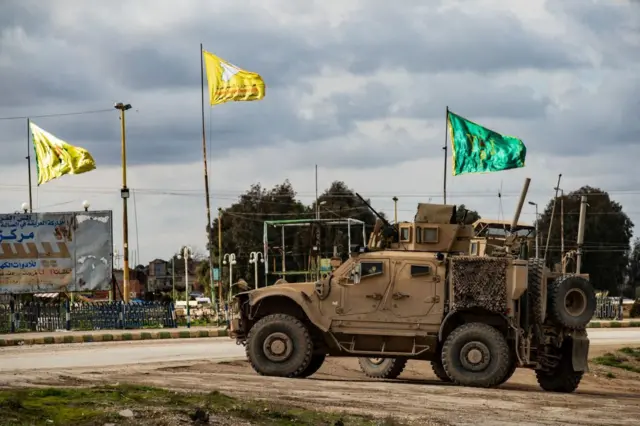 دورية من المركبات العسكرية الأمريكية بالقرب من الأعلام الصفراء لقوات سوريا الديمقراطية (SDF) والعلم الأخضر لقوات حماية المرأة (YPJ) التابعة لها ببلدة تل تمر شمال في محافظة الحسكة شمال شرق سوريا على طول الحدود مع تركيا.