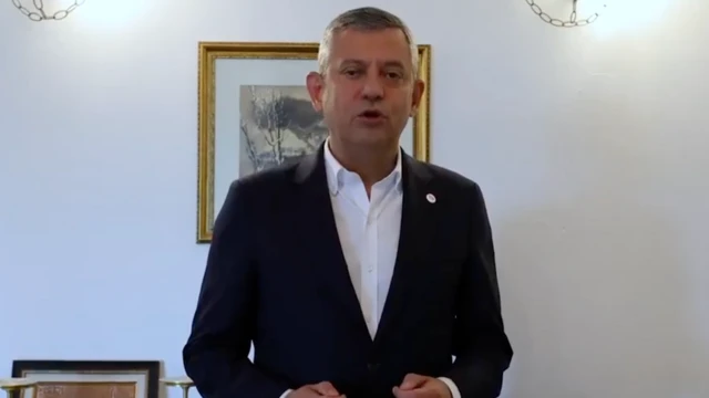 Özgür Özel siyah beyaz takım elbise giyiyor. Kravat takmamış, bu videoyu bir odada çekmiş