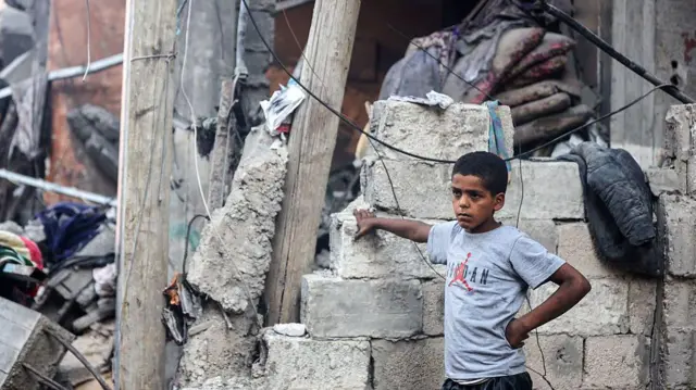 طفل فلسطيني ينظر إلى رجل يبحث عن ناجين بين أنقاض مبنى في مخيم الشاطئ للاجئين بمدينة غزة، في 9 يوليو/تموز 2025، والذي استُهدف بغارة إسرائيلية.