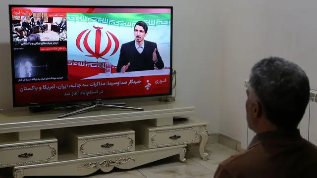 तेहरान में एक ईरानी निवासी न्यूज़ चैनल पर अमेरिका और ईरान के बीच वार्ता की ख़बरें देखता हुआ