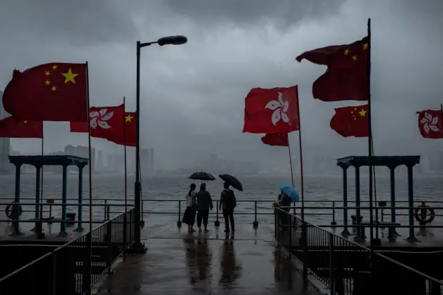 Người dân nhìn ra cảng Victoria trong cơn dông. Xung quanh cắm cờ Trung Quốc và Hong Kong nhân dịp kỷ niệm 25 năm Anh trả thành phố về tay đại lục.