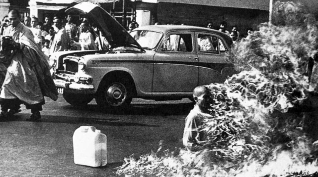 Sous le regard des gens présents, une homme assis à même le sol est en train de brûler vif.