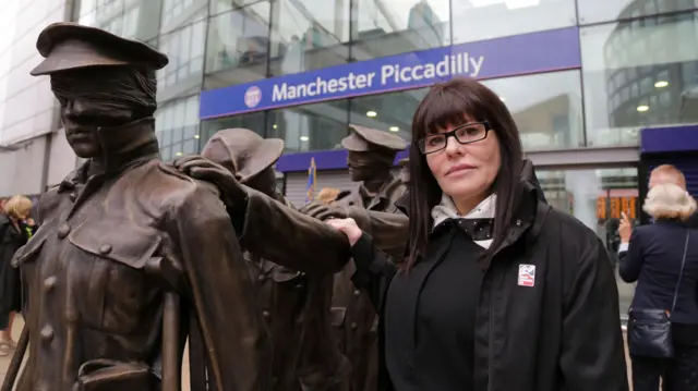 Johanna Domke-Guyot tiene el pelo largo y oscuro y lleva gafas. Su mano se apoya en el brazo de un hombre, parte de su escultura de bronce que representa a soldados ciegos.