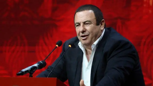 Tsarukyan kürsüde konuşuyor. Üzerinde siyah bir ceket ve beyaz gömlek var. Kıravat takmıyor.