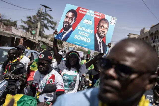 Un partisan de la coalition Diomaye Président brandit une affiche avec le candidat présidentiel Bassirou Diomaye Faye et le leader de l'opposition Ousmane Sonko lors d'un rassemblement de campagne à Dakar le 10 mars 2024. 